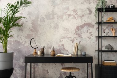 Concrete interior of home office with copy space, black desk, office accessories and plants. Rack with personal accessories. Home decor. Template. 