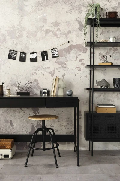 Concrete interior of home office with black desk, office accessories, lamp. Rack with personal accessories. Home decor. Template.