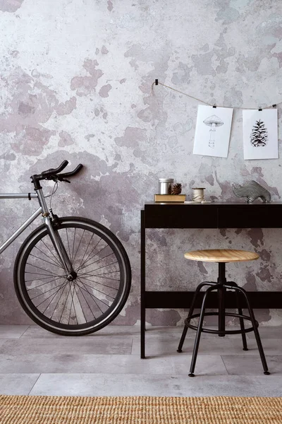 Concrete interior of home office with black desk, office accessories, bicycle. Rack with personal accessories. Home decor. Template.