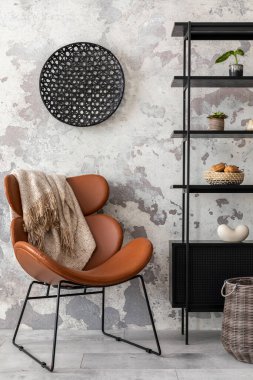 The stylish composition of wabi sabi interior with black rack, brown armchair with plaid and personal accesoories. Grey concrete wall. Home decor. Template. 