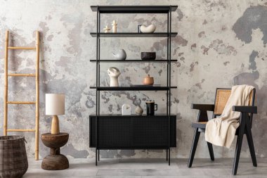 The stylish composition of wabi sabi interior with black rack, rattan armchair, carpet, coffee table and personal accesoories. Grey concrete wall. Home decor. Template. 