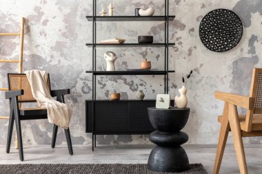 The stylish composition of wabi sabi interior with black rack, rattan armchair, carpet, coffee table and personal accesoories. Grey concrete wall. Home decor. Template. 