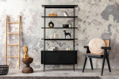 The stylish composition of wabi sabi interior with black rack, rattan armchair, carpet, coffee table and personal accesoories. Grey concrete wall. Home decor. Template. 