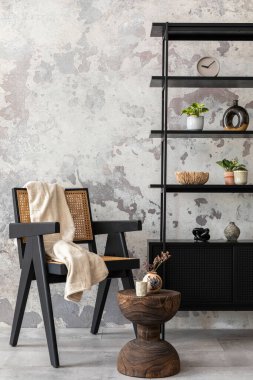 The stylish composition of wabi sabi interior with black rack, rattan armchair, carpet, coffee table and personal accesoories. Grey concrete wall. Home decor. Template.