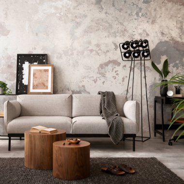 The stylish compostion at concrete living room interior with design gray sofa, wooden coffee table, desk and elegant personal accessories. Loft and industrial interior. Home decor. Template.