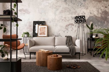 The stylish compostion at concrete living room interior with design gray sofa, wooden coffee table, desk and elegant personal accessories. Loft and industrial interior. Home decor. Template.