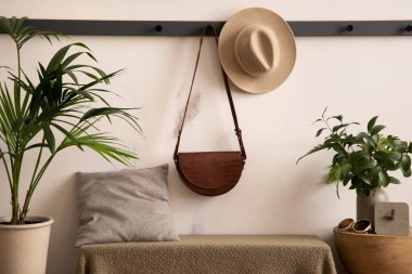 The stylish composition of cosy entryway with hanger, bench with green plaid and pillow, plants and personal accessories. Beige wall. Home decor. Template. 