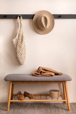 The stylish composition of cosy entryway with grey bench, hanger and personal accessories. Beige wall. Home decor. Template. 