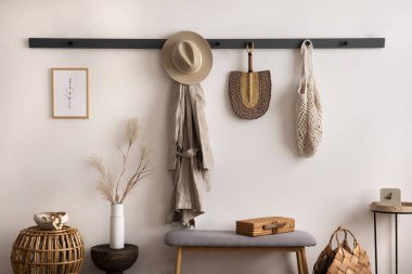 The stylish composition of cosy entryway with wooden basket, carpet, hanger and personal accessories. Beige wall. Home decor. Template. 