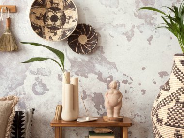 The stylish ethnic composition at living room interior with design, colorful baskets, bench and elegant personal accessories. Grey concrete wall. Cozy apartment. Home decor. 