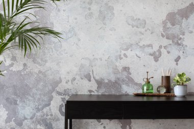 Concrete interior of home office with copy space. Black desk, image, lamp and office accessories. Grey concrete wall. Home decor. Template. 