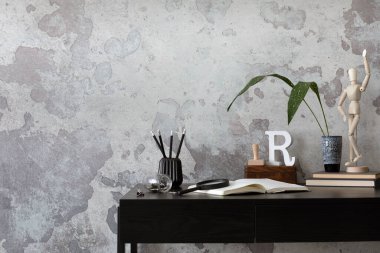 Concrete interior of home office with copy space. Black desk, image, lamp and office accessories. Grey concrete wall. Home decor. Template. 