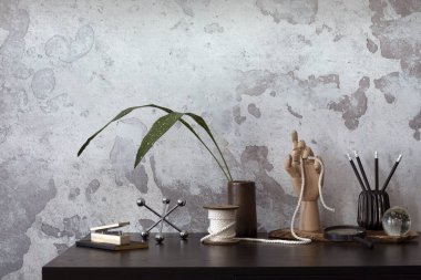 Concrete interior of home office with black desk, leaves and office accessories. Grey concrete wall. Home decor. Template. 