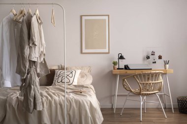 Stylish composition of cozy bedroom with mock up, beige bedding, plants, armchair and wooden desk. Mock up poster with wooden frame. Home decor. Template. 