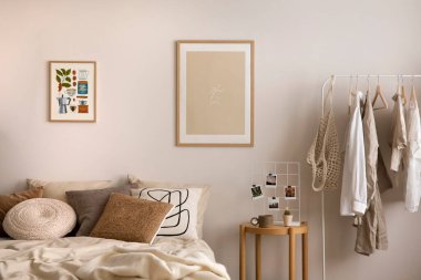Stylish composition of cozy bedroom with mock up, beige bedding, and wooden armchair. Mock up poster with wooden frame. Home decor. Template. 