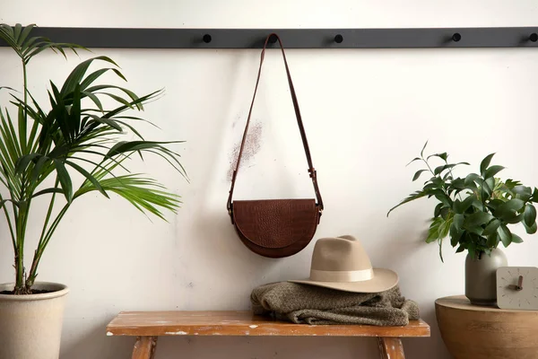 The stylish composition of cosy entryway with wooden bench, coffee table, bag hanger and personal accessories. Beige wall. Home decor. Template.