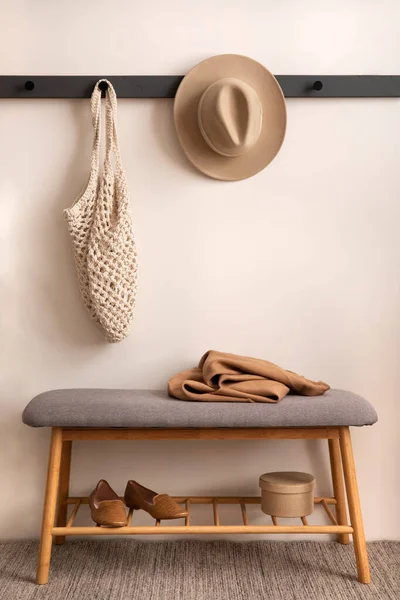 The stylish composition of cosy entryway with grey bench, hanger and personal accessories. Beige wall. Home decor. Template.