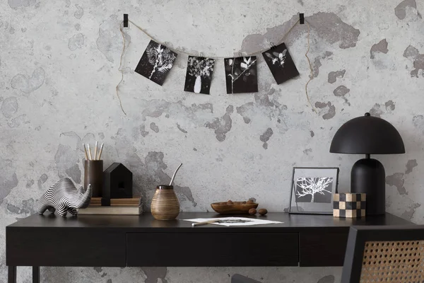 Concrete interior of home office with black desk, image, lamp and office accessories. Grey concrete wall. Home decor. Template.