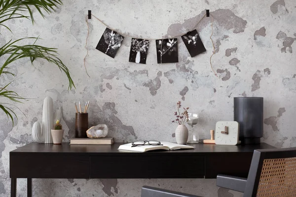 Concrete interior of home office with black desk, image, lamp and office accessories. Grey concrete wall. Home decor. Template.