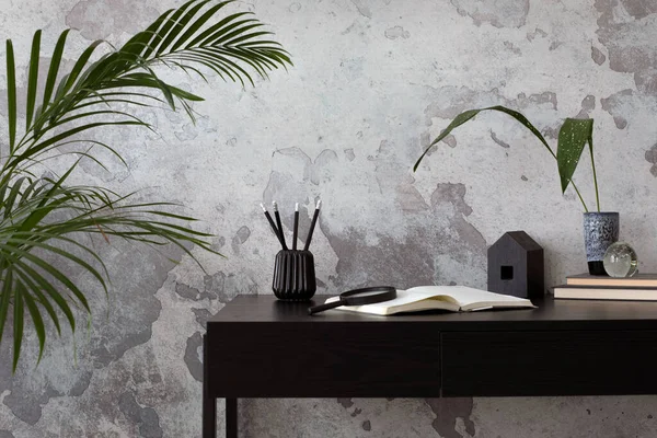 Concrete interior of home office with black desk, flowers,  and office accessories. Grey concrete wall. Home decor. Template.