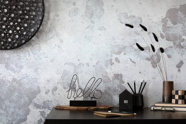 Concrete interior of home office with black desk, ornaments on the wall and office accessories. Grey concrete wall. Home decor. Template.