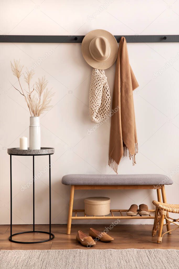 The stylish composition of cosy entryway with grey bench, coffee table, hanger and personal accessories. Beige wall. Home decor. Template. 