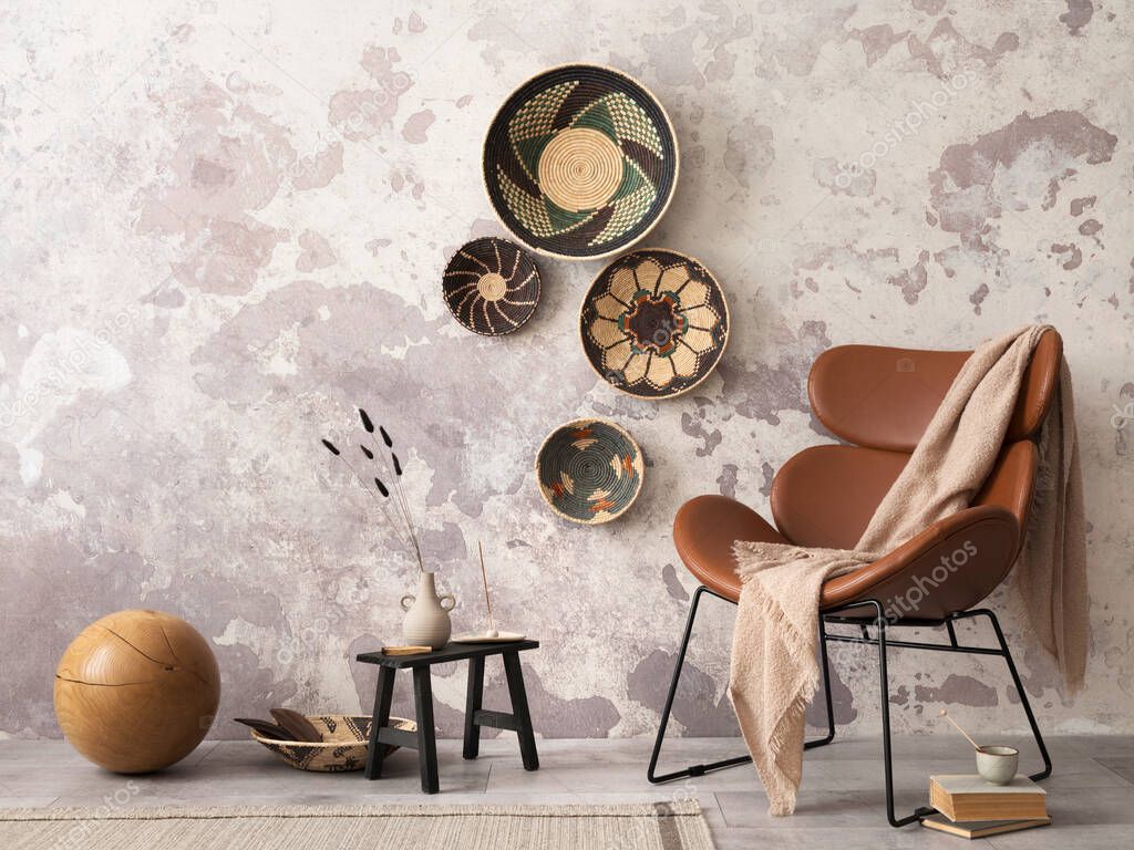 The stylish ethnic composition at living room interior with design brown armchair, colorful baskets,  and elegant personal accessories. Grey concrete wall. Cozy apartment. Home decor. 