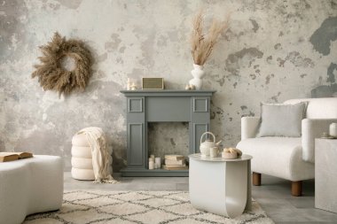 The stylish living room interior with grey fireplace, white armchair, concrete wall and dried flowers. Grey floor with beige carpet. Home decor. Template. 
