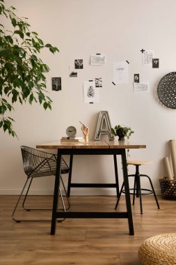 The stylish composition of cozy office interior with metal chair, wooden table, plants, pictures and personal accessories. Home decor. Template. 