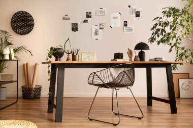 The stylish composition of cozy office interior with metal chair, wooden table, plants poster and personal accessories. Home decor. Template. 