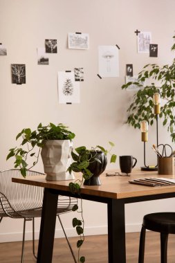 The stylish composition of cozy office interior with metal chair, wooden table, plants, pictures and personal accessories. Homne decor. Template. 