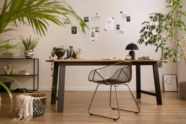 The stylish composition of cozy office interior with metal chair, wooden table, plants poster and personal accessories. Homne decor. Template. 