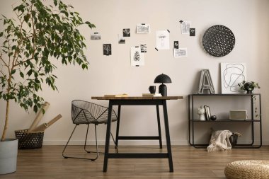 The stylish composition of cozy office interior with metal chair, wooden table, plants poster and personal accessories. Home decor. Template. 
