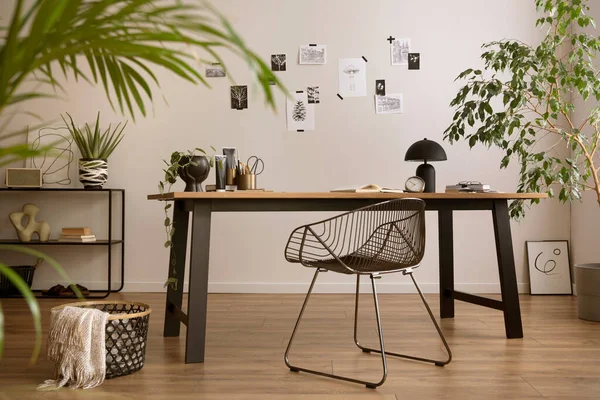The stylish composition of cozy office interior with metal chair, wooden table, plants poster and personal accessories. Homne decor. Template. 
