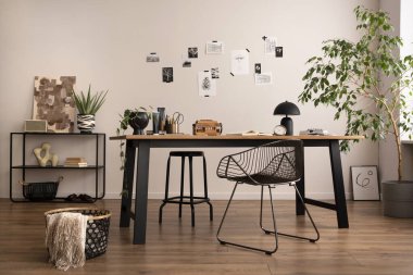 The stylish composition of cozy office interior with metal chair, wooden table, plants poster and personal accessories. Home decor. Template. 