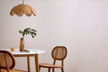 The stylish dining room with copy space, round table, rattan chair, lamp and kitchen accessories. Leaf in a vase. Home decor. Template. 