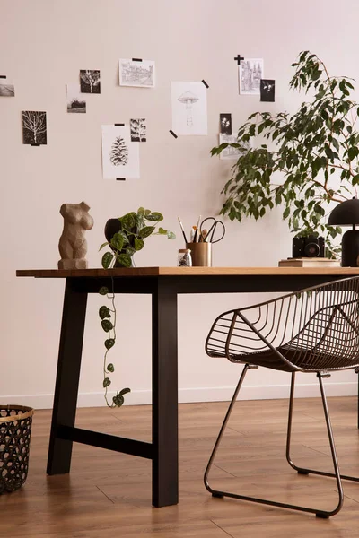 The stylish composition of cozy office interior with metal chair, wooden table, plants poster and personal accessories. Home decor. Template. 