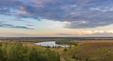 Tepenin üzerinde günbatımının canlı renkleri. Akşamları renkli manzara, tepeleri ve nehri olan altın bulutları olan muhteşem mavi gökyüzü. Doğanın büyülü anı. 