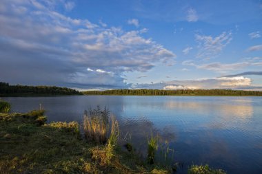 Akşamları nehrin üzerinde bulutlu bir gökyüzü. Bulutları ve nehri olan resim gibi bir manzara. Ön planda parlak yeşil çimenler.