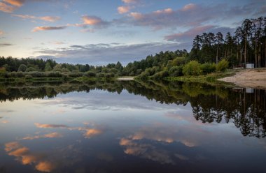 Akşamları nehir kıyısında yaz manzarası. Dramatik bulutlar suya yansıyor. Gün batımından sonra manzarada yoğun renkler.