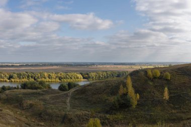 Çayır manzarası ve kırsal alanların sonsuz genişliği. Uzakta bir nehir olan sonbahar manzarası. Güneş bir sonbahar günü tarlalarda ve tepelerde bulutların arasından parlar..