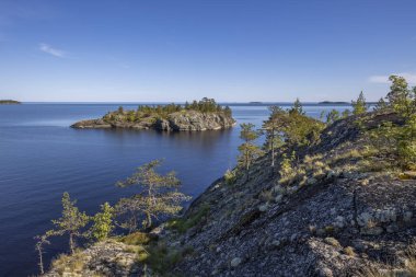Göl üzerinde taşlarla kaplı bir orman manzarası. Gölde güneşli bir gün. Suyun içindeki gökyüzünün yansıması. Taş üstünde çam. Kuzeyin doğası.. 