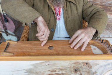 Etnik giyimli bir adam antik bir müzik aleti çalar. Kahverengi keten ceketli bir adam psaltery çalıyor..