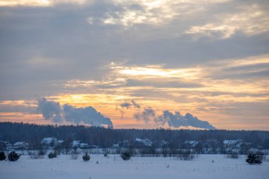 Kış minimalist manzarası gökyüzünde renkli bulutlar ve ufukta tüten bacalar. kış turizmi
