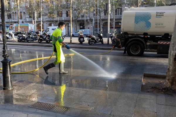 Barselona, İspanya - 20 Aralık 2021. Bir adam hortumla sokakları suyla yıkıyor. Kamu hizmeti sabahın erken saatlerinde şehir caddesini temizler.