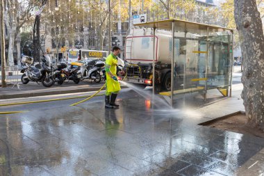 Barselona, İspanya - 20 Aralık 2021. Bir adam hortumla sokakları suyla yıkıyor. Kamu hizmeti sabahın erken saatlerinde şehir caddesini temizler.