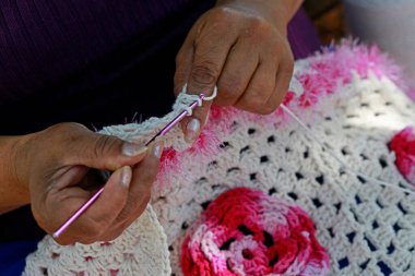 Pembe ve beyaz renklerde örgü ören kadın elleri