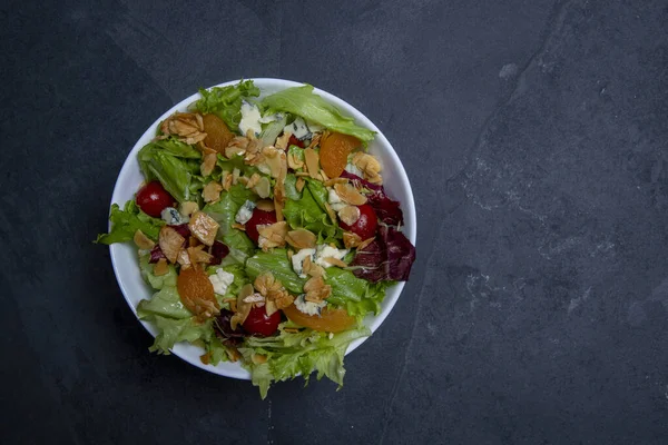 Bir tabak yeşil yapraklı, domatesli, peynirli, bademli ve kayısılı salata. boşluk metni