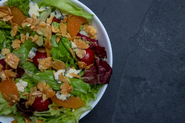 Bir tabak yeşil yapraklı, domatesli, peynirli, bademli ve kayısılı salata. boşluk metni