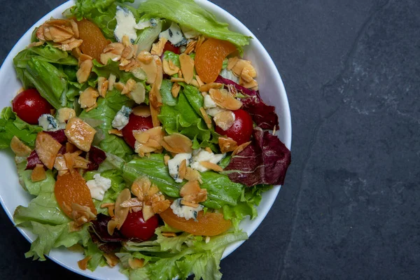 Bir tabak yeşil yapraklı, domatesli, peynirli, bademli ve kayısılı salata. Metin için boşluk